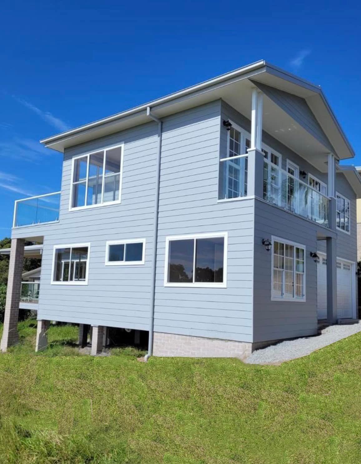 Two-story blue house with white trim and a balcony — Mid North Coast Drafting & Construction in Nabiac, NSW