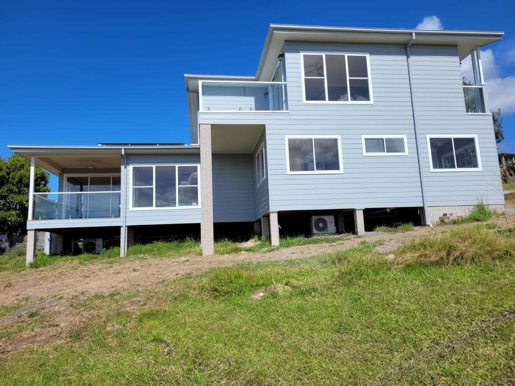 Two-story Blue House With White Trim and Glass Balconies — Mid North Coast Drafting & Construction in Forster, NSW