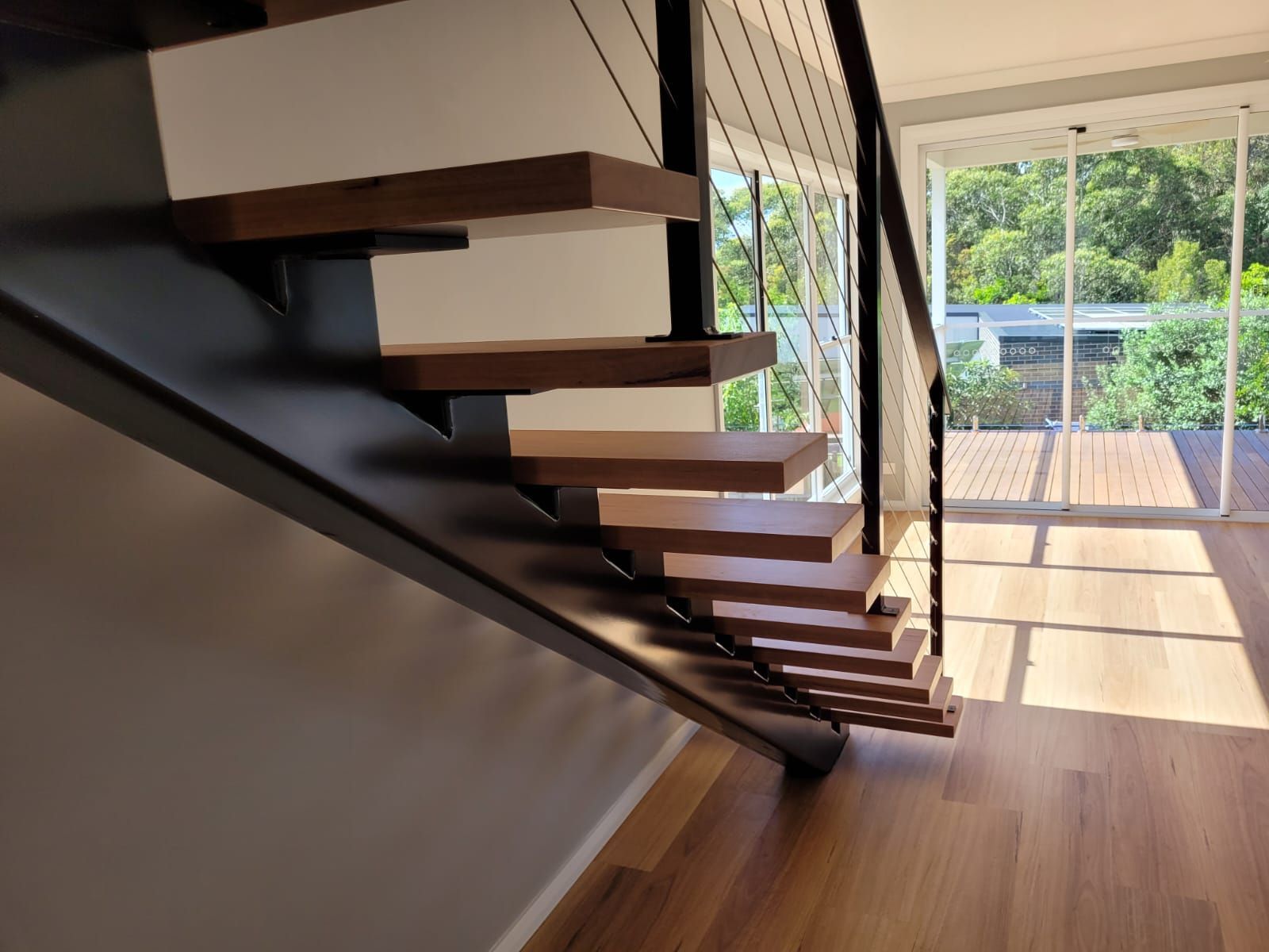 Floating Wooden Staircase With Black Metal Support and Cable Railing — Mid North Coast Drafting & Construction in Taree, NSW
