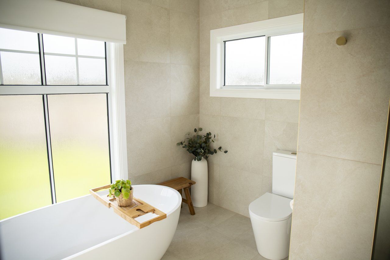 Modern Bathroom With White Bathtub, Toilet, and Neutral Tile — Mid North Coast Drafting & Construction in Taree, NSW