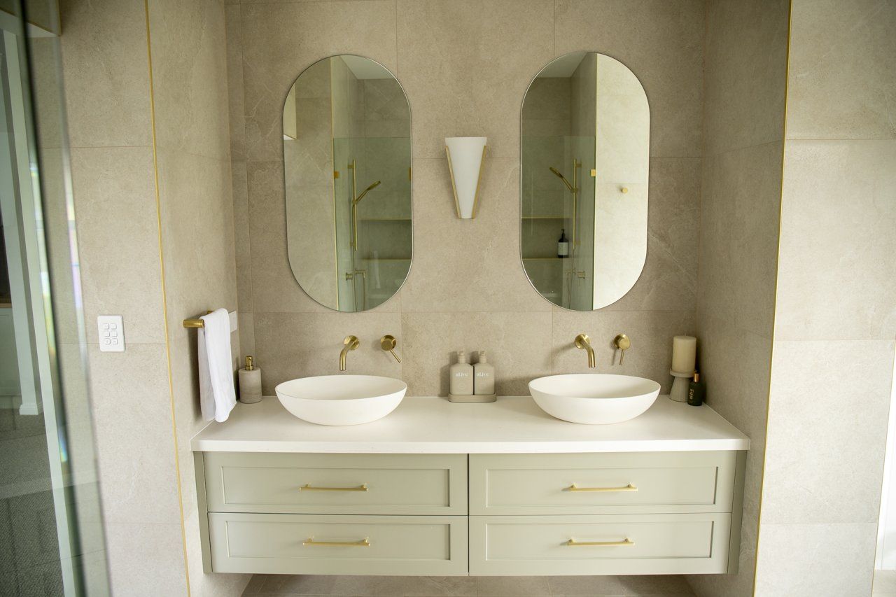 Bathroom With Two Oval Mirrors, Sinks, and Gold Fixtures — Mid North Coast Drafting & Construction in Taree, NSW