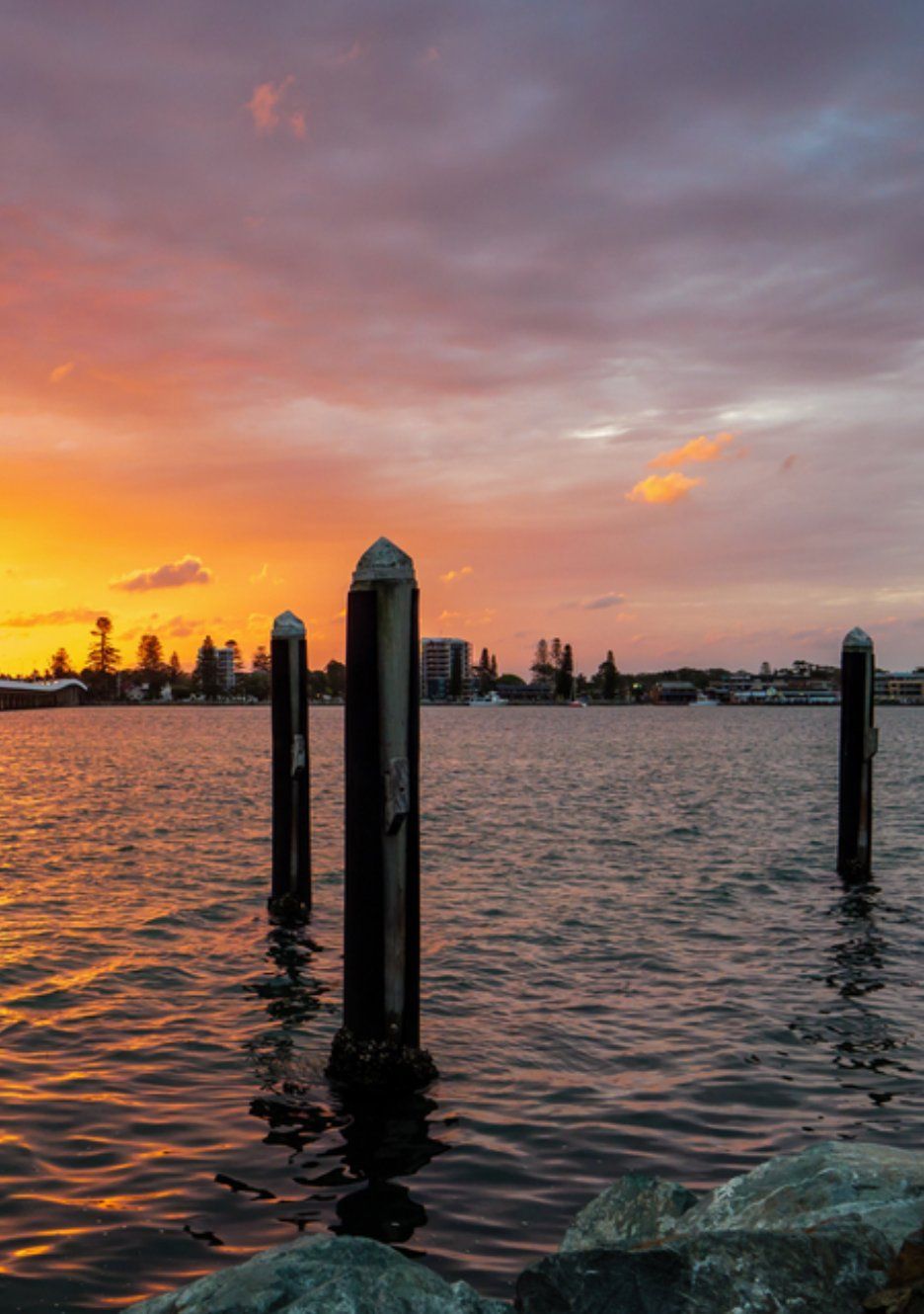 Sunset Over Water With Pilings and Horizon Buildings — Mid North Coast Drafting & Construction in Forster, NSW