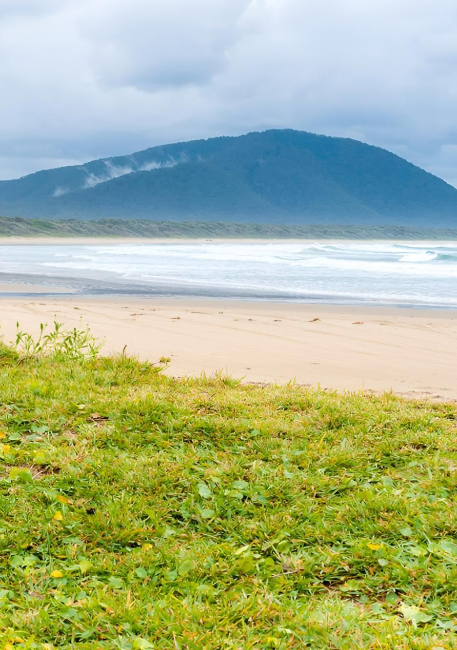 Beach With Sand, Green Grass, and Mountain Under Cloudy Sky — Mid North Coast Drafting & Construction in Diamond Beach, NSW