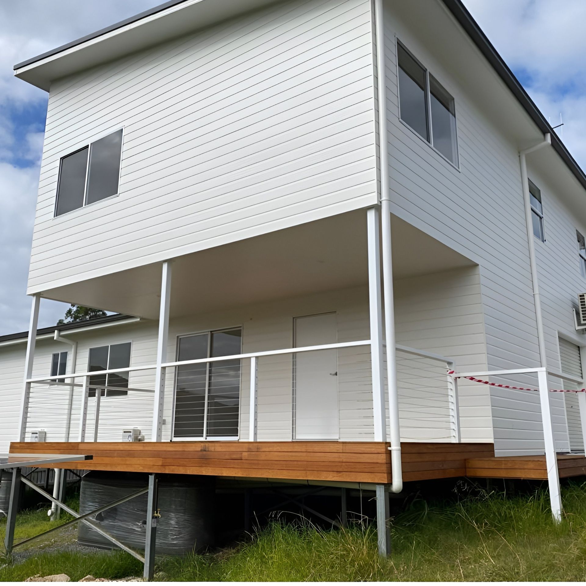 White Two-Story House With Wooden Deck and Glass Railing — Mid North Coast Drafting & Construction in Taree, NSW