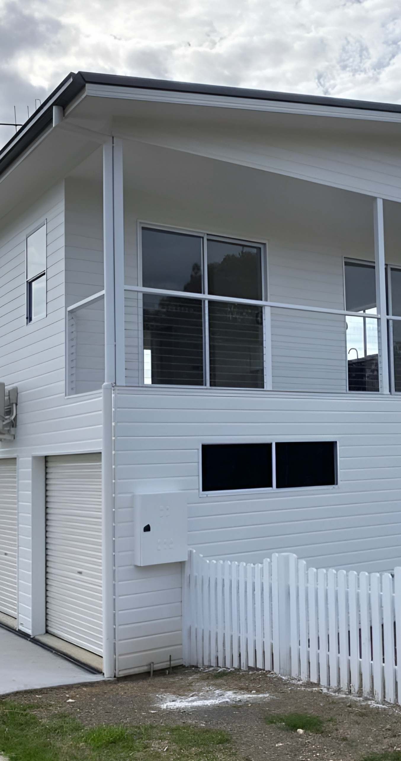 White Two-Story House With Balcony, Garage, and Picket Fence — Mid North Coast Drafting & Construction in Diamond Beach, NSW