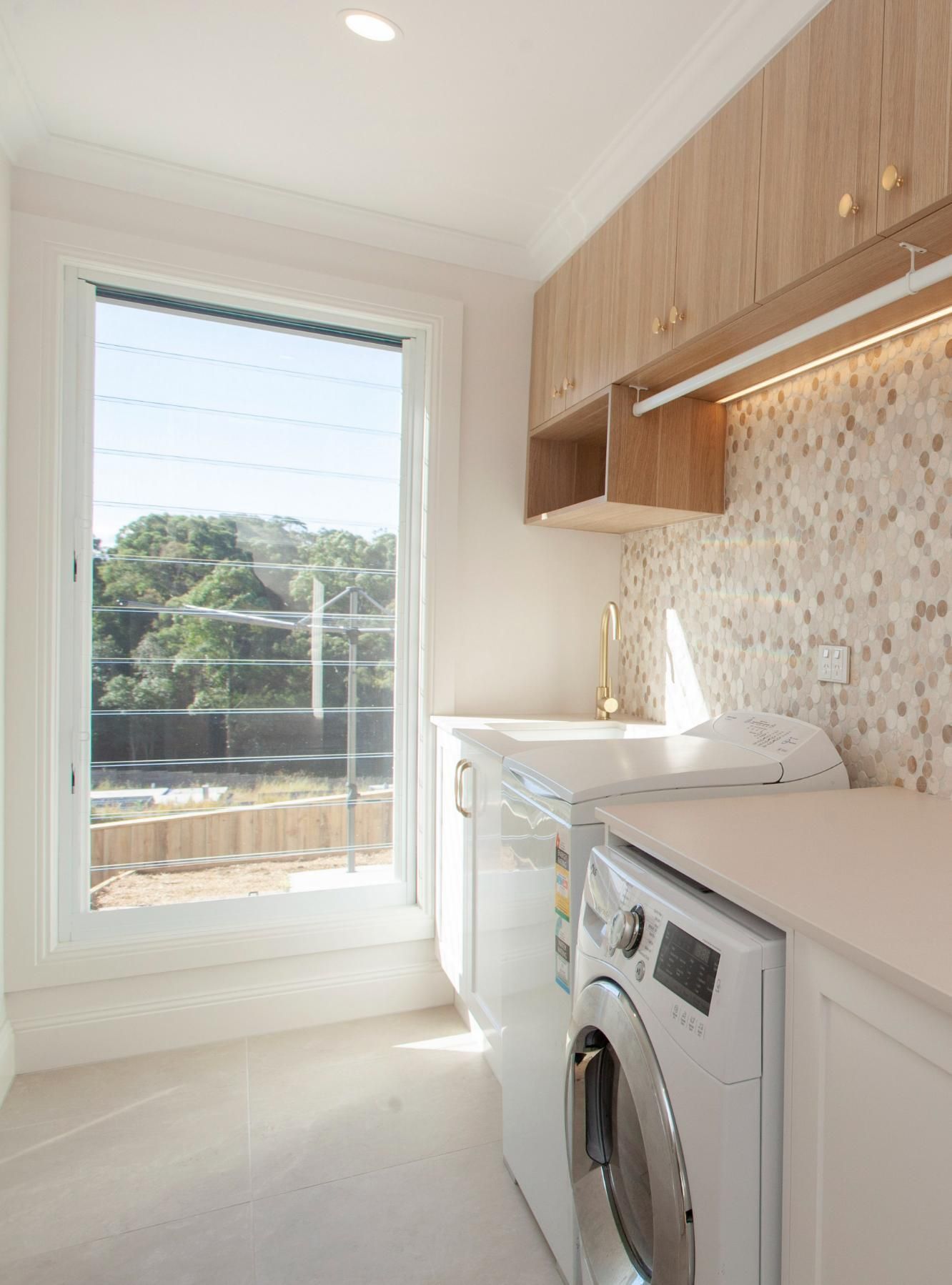 Bright Laundry Room With Window, Washer, and Wood Cabinets — Mid North Coast Drafting & Construction in Harrington, NSW