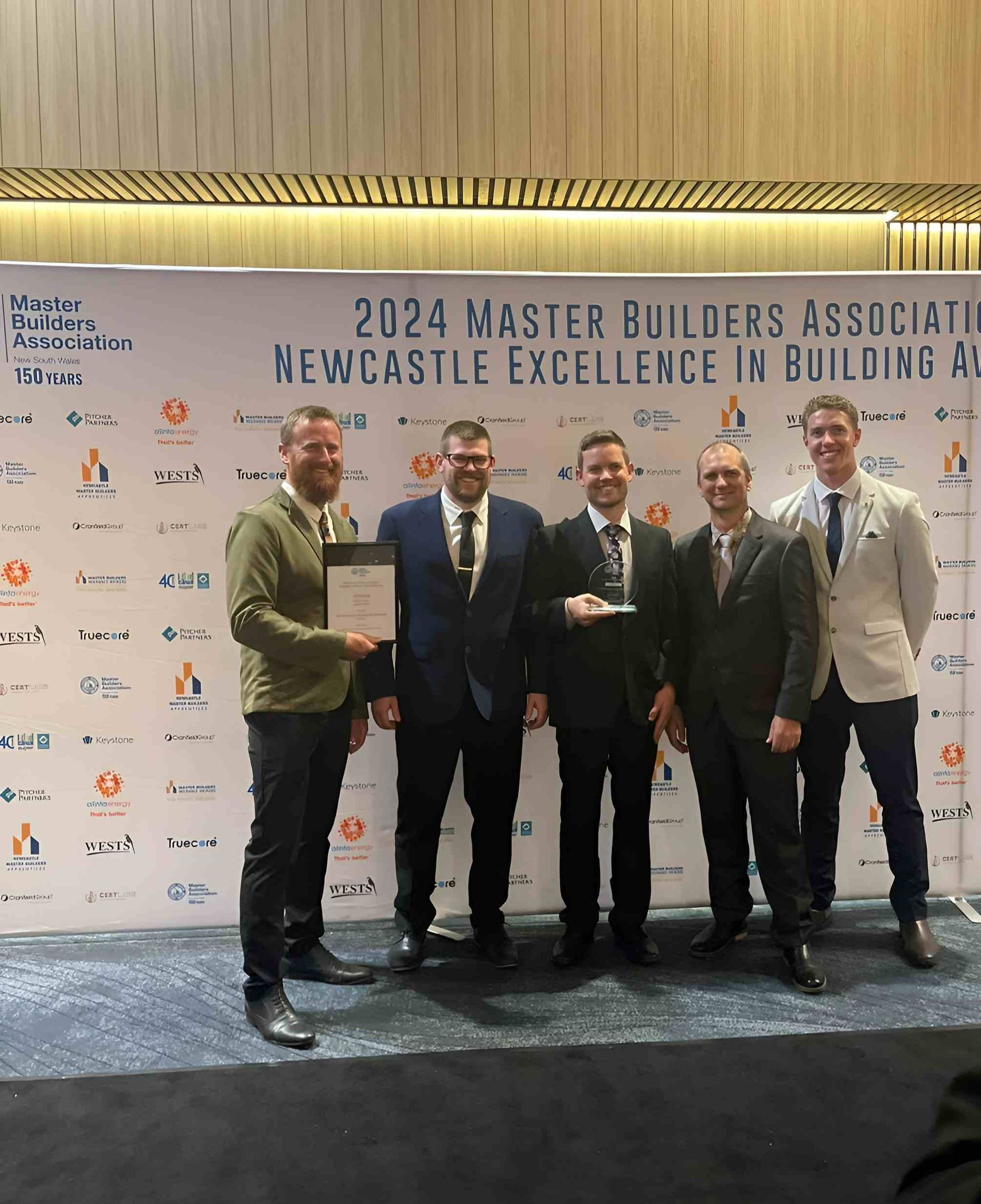 Team Standing Behind Desk With Logo — Mid North Coast Drafting & Construction in Taree, NSW