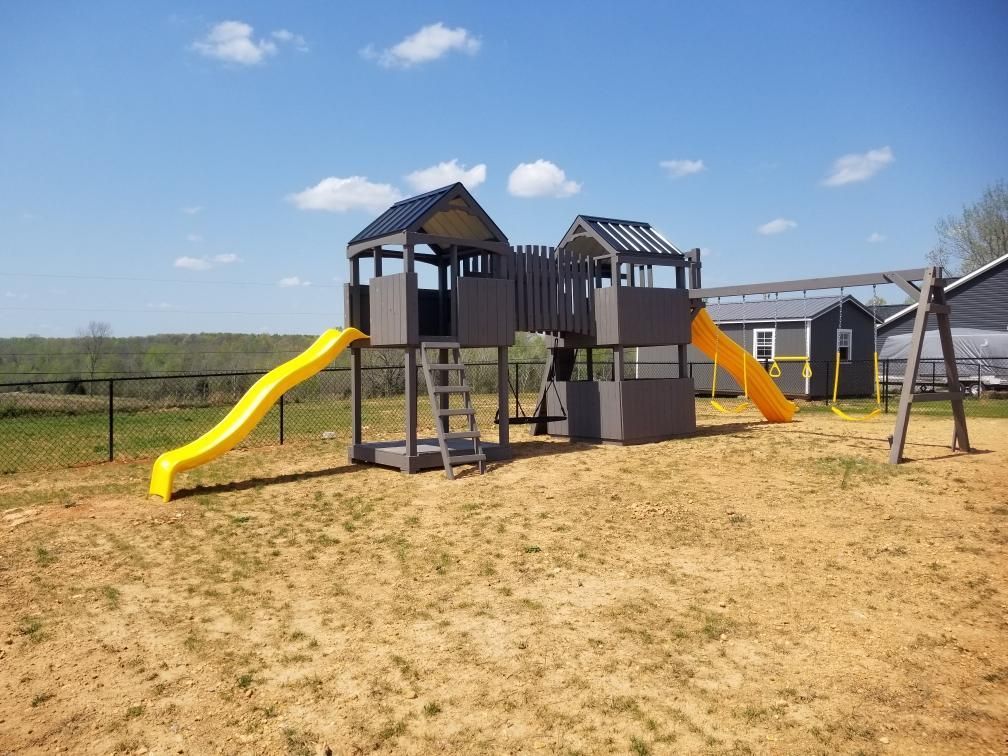 Playground structure with two yellow slides and a set of swings on a sunny day.