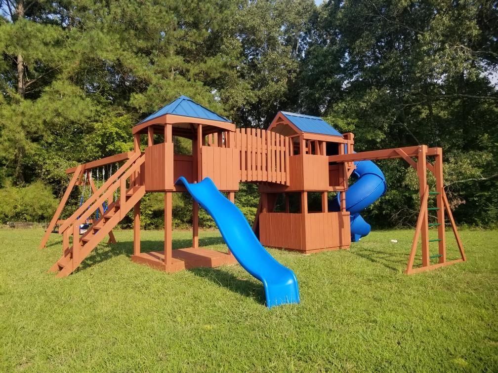 A wooden playground set with a blue slide and swings in a grassy field.