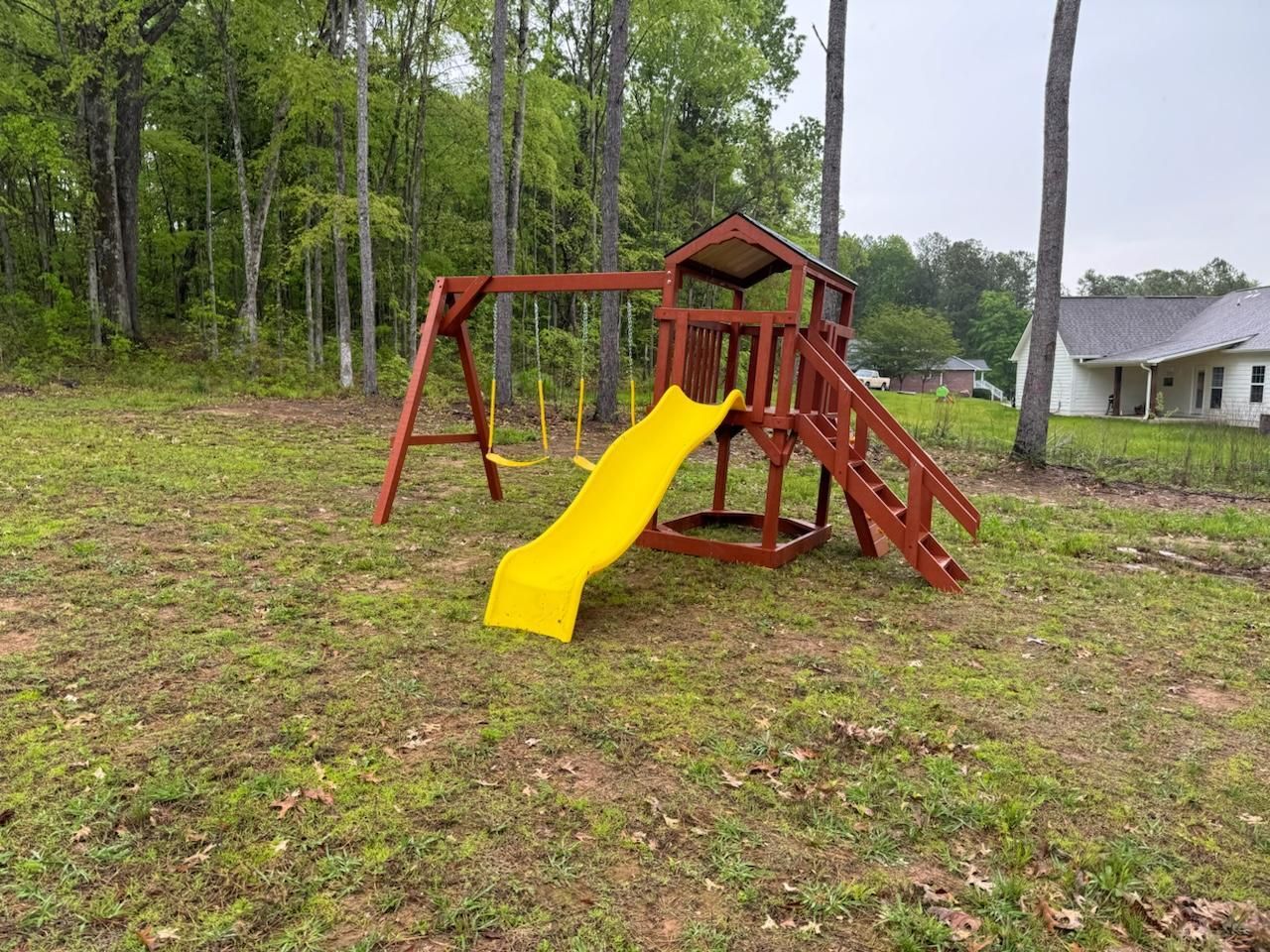 Wooden playset with yellow slide and swings in a grassy yard.