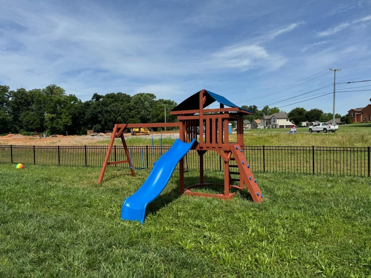 Wooden playset with blue slide, swings, and climbing ladder in a grassy backyard.