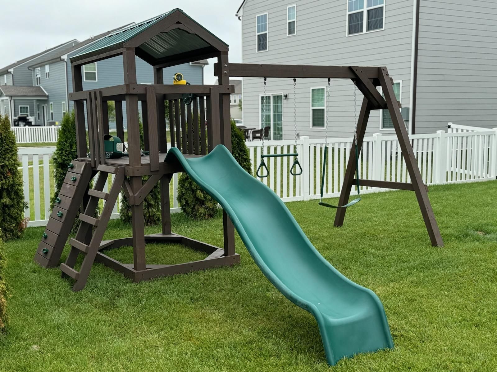 A playground set with a slide and swings in a backyard.