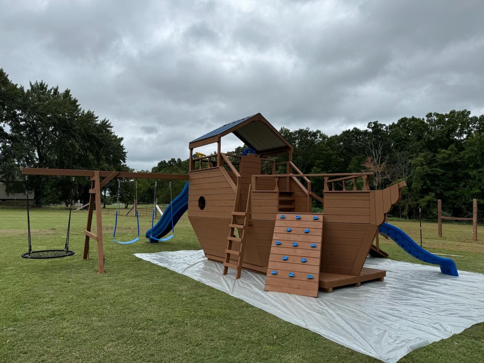 Backyard wooden playset with blue slides and swings on a grassy lawn