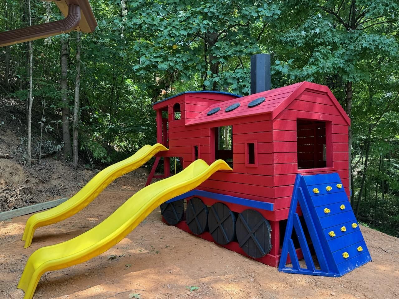 A red train playground with yellow slides and a climbing wall