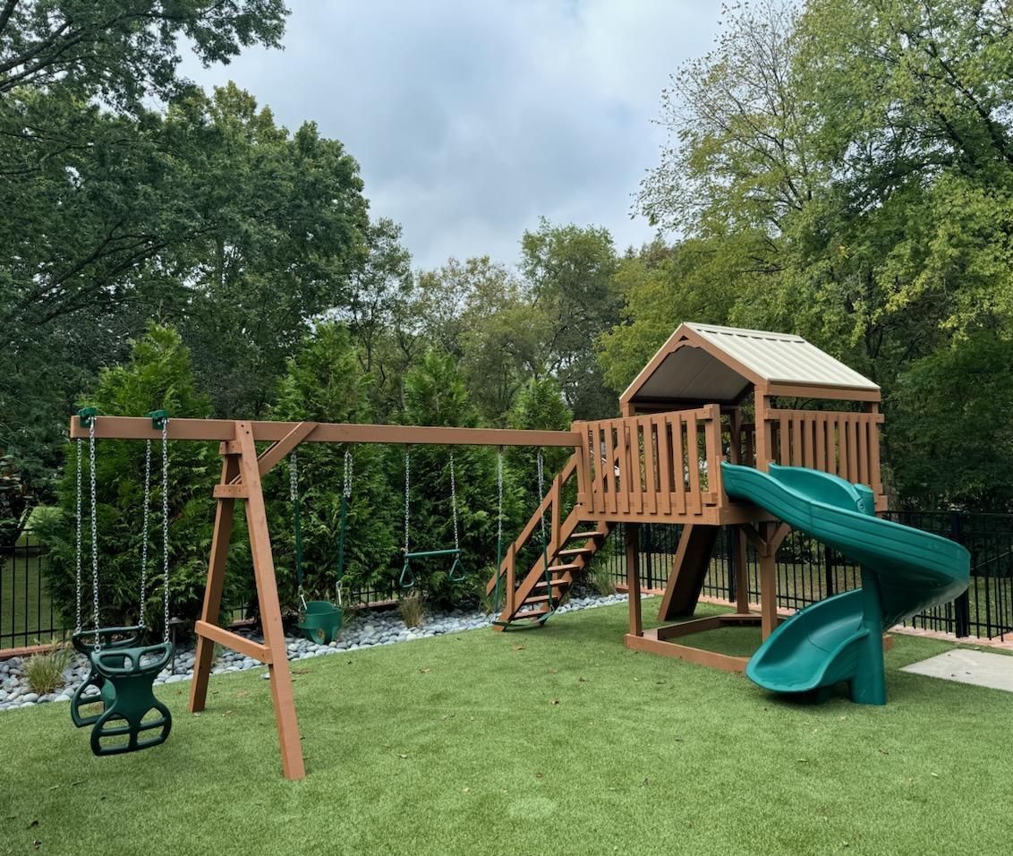 A wooden swing set with a green slide and swings in a backyard.