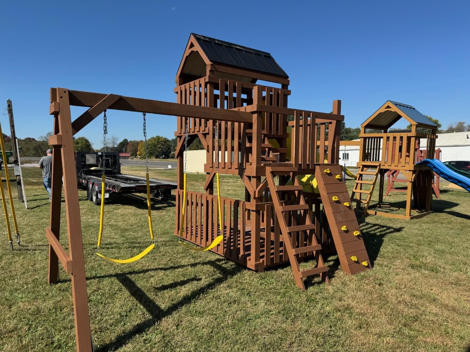 Wooden playset with swings, climbing wall, slide, and two towers on a grassy lawn.