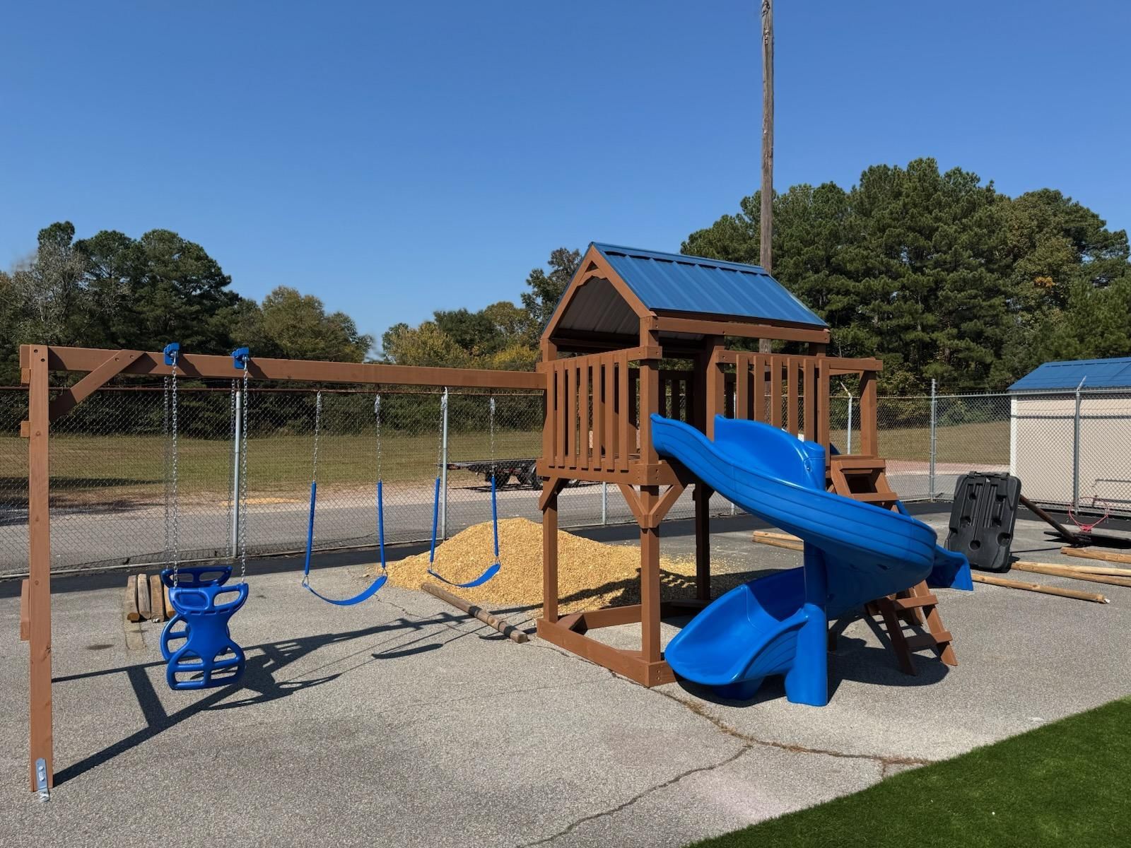 A wooden playground with a blue slide and swings