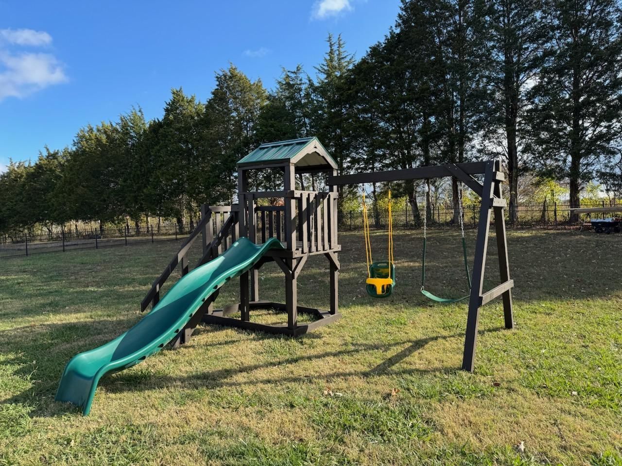 Wooden backyard playset with a slide, swing, and climbing structure on a grassy lawn.