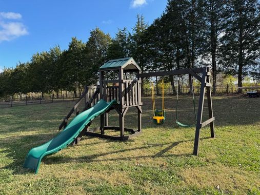 Wooden backyard playset with a slide, swing, and climbing structure on a grassy lawn.