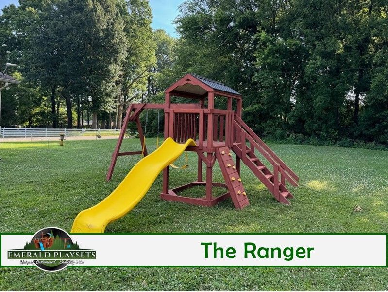 Wooden playset in a grassy yard, featuring a slide, climbing wall, swing, and tower.