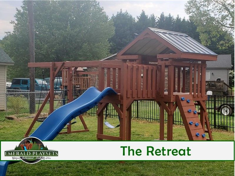 Playground structure with blue slide, swings, climbing wall, and a wooden playhouse in a grassy backyard.