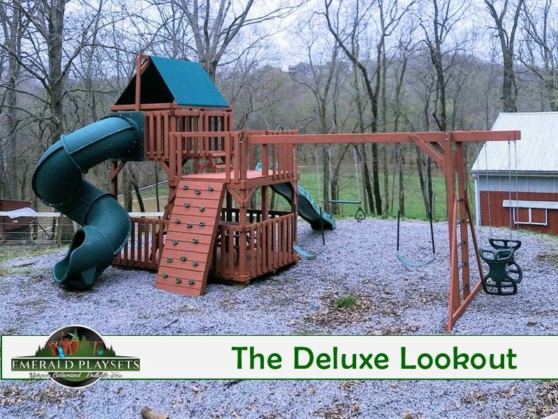 Wooden playground with slides, climbing wall, and swing set in a wooded area.