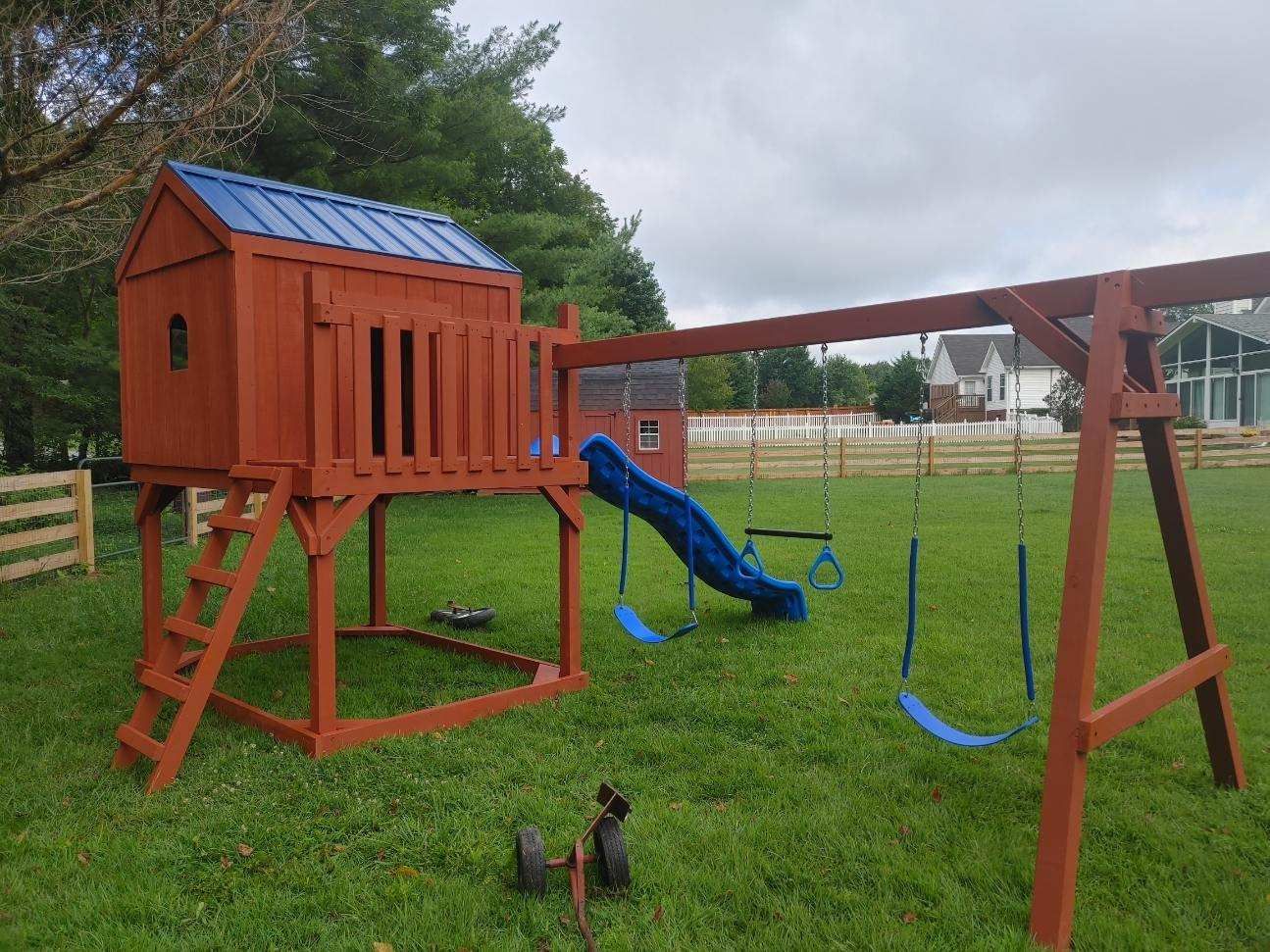 Wooden playground structure in a grassy yard, featuring a playhouse, swings, and a slide.