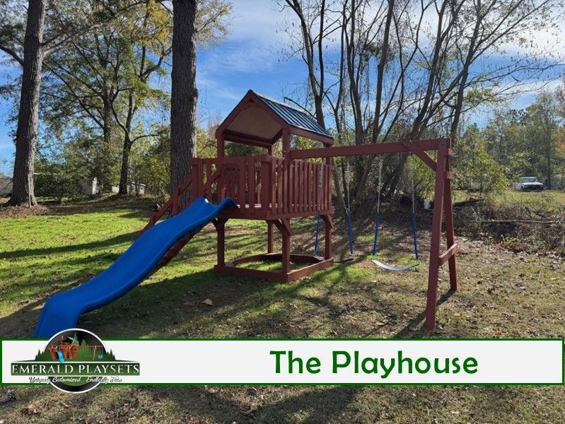Playhouse with a blue slide, swing set, and brown wooden structure, set in a grassy yard.