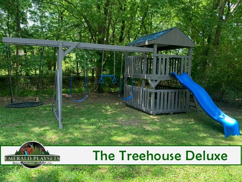 Gray wooden playset with swings, a slide, and a treehouse structure in a grassy yard.