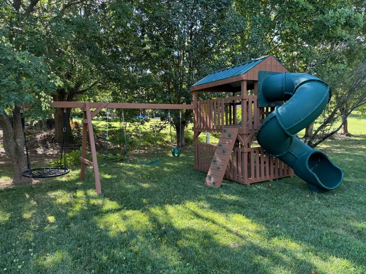 A wooden swing set with a green slide and swings in a backyard.