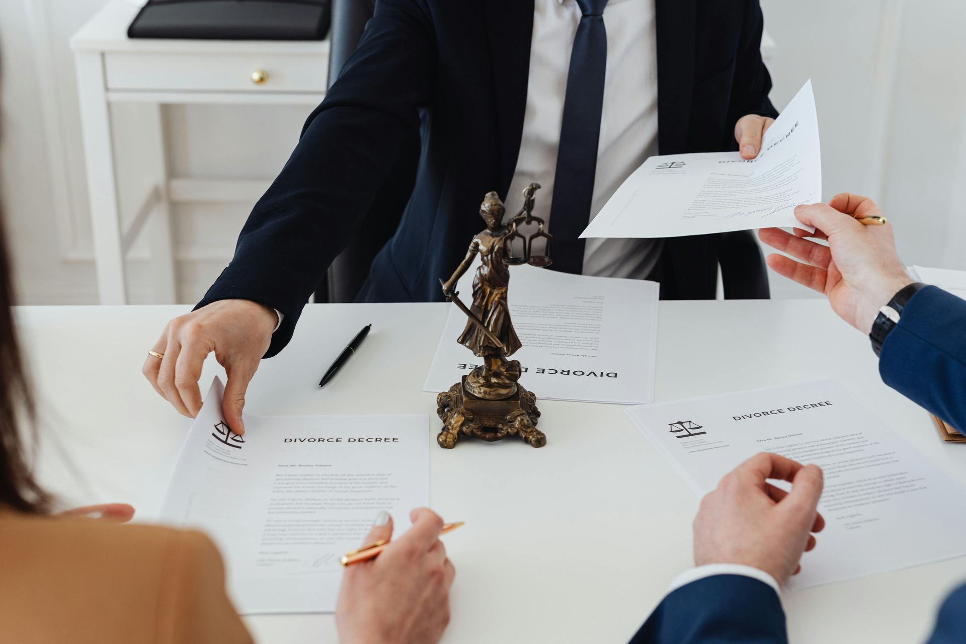 People at table with documents, a justice statue, and a pen; legal setting.