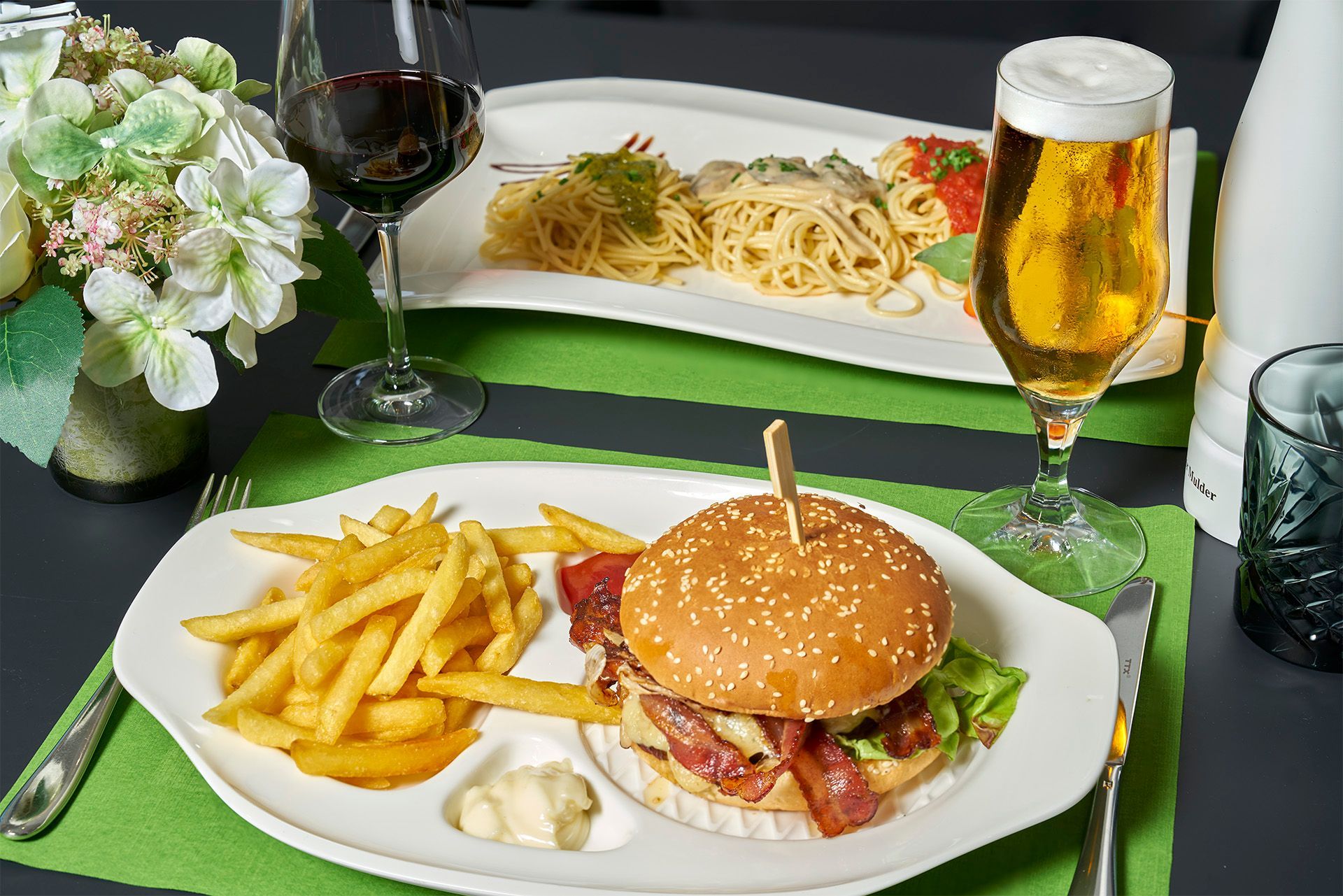 Ein Teller mit Essen, einem Hamburger, Pommes Frites und einem Glas Bier auf einem Tisch.