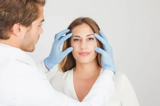 A man in blue gloves is examining a woman 's face.