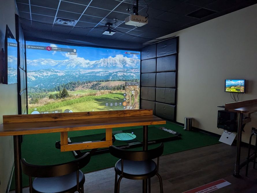 A room with a table and chairs and a large screen on the wall.