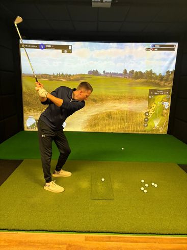 Golf club poised to hit a bright yellow golf ball on green turf, with a shoe in the background.
