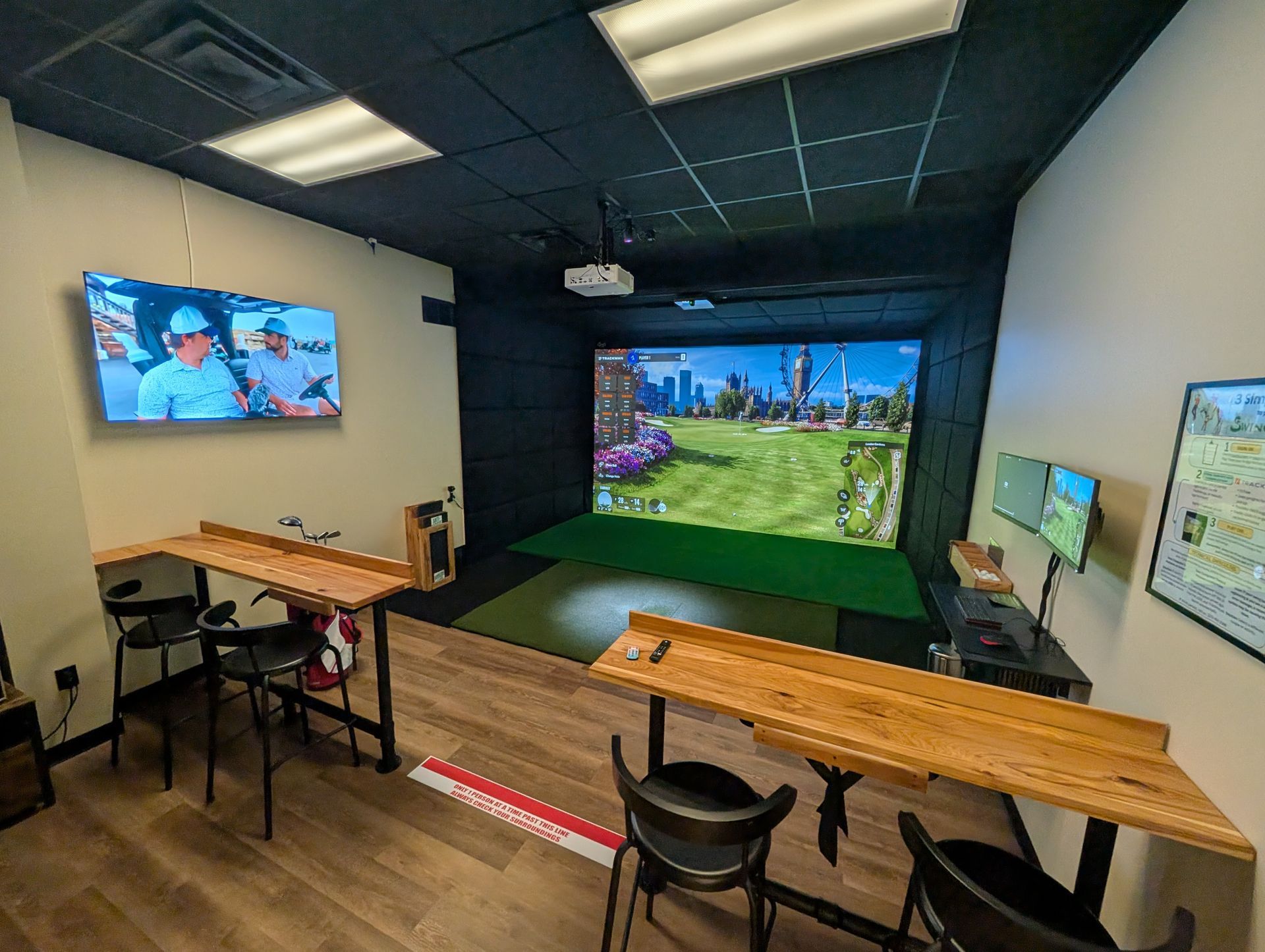 Golf simulator room with screens showing a course, bar seating, and overhead lighting.