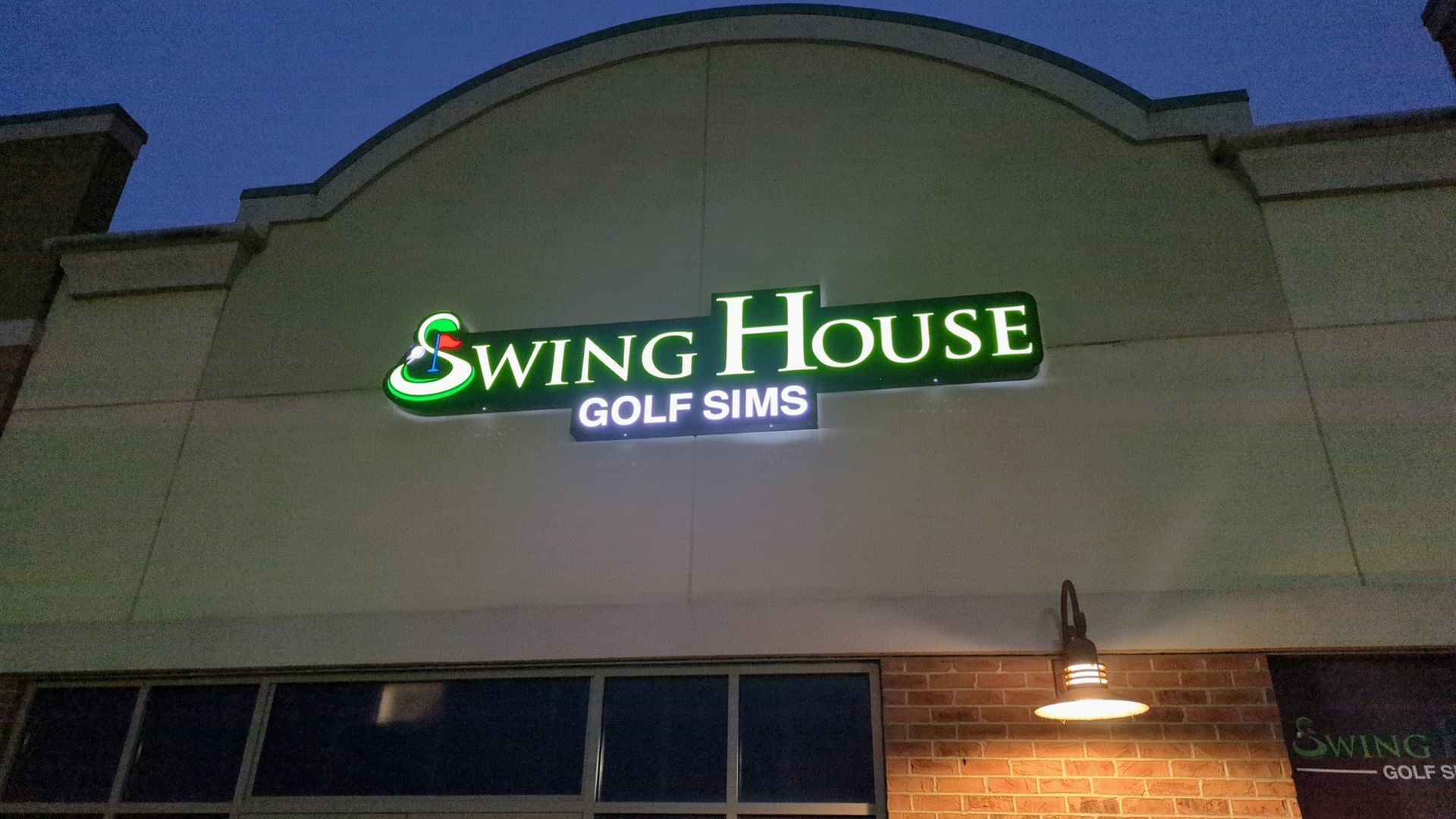 A swing house golf sims sign is lit up at night