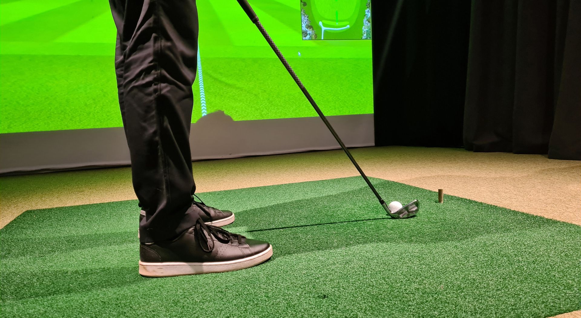 Golfer setting up for a shot, club head at the ball. On green turf, green background.