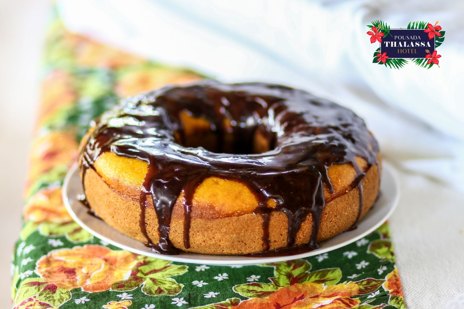 Um bolo com cobertura de chocolate está em um prato branco sobre uma mesa.