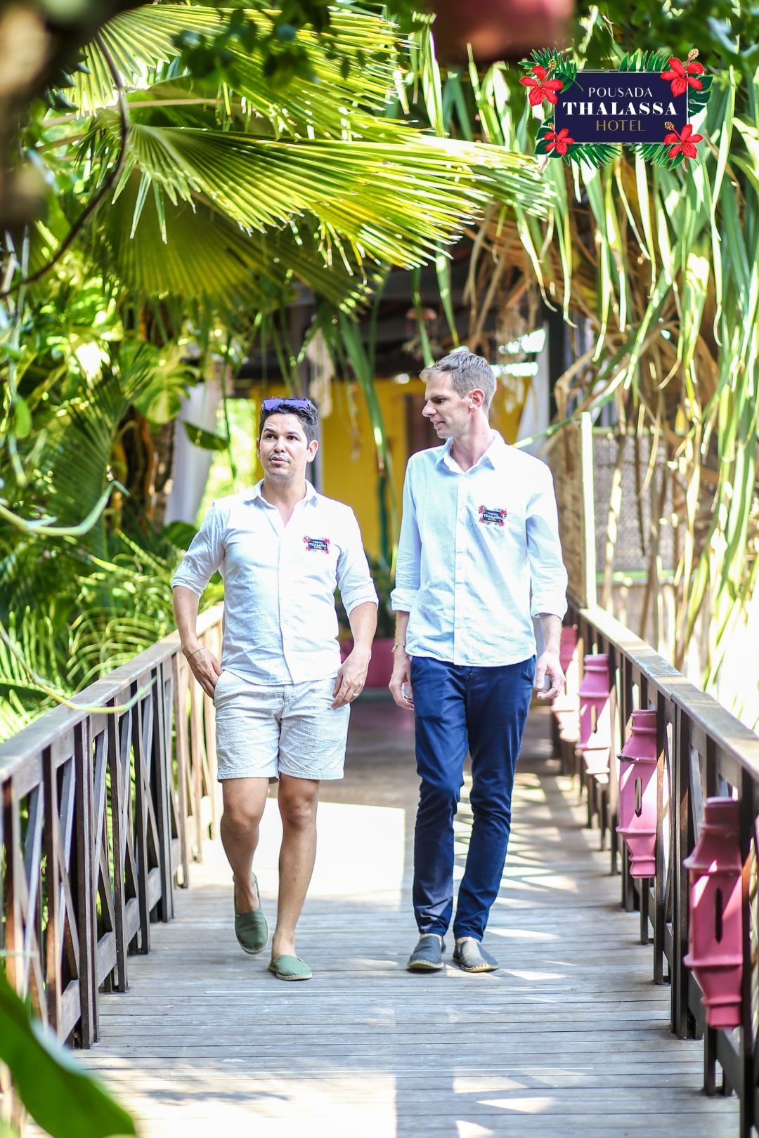 Dois homens estão atravessando uma ponte de madeira de mãos dadas.