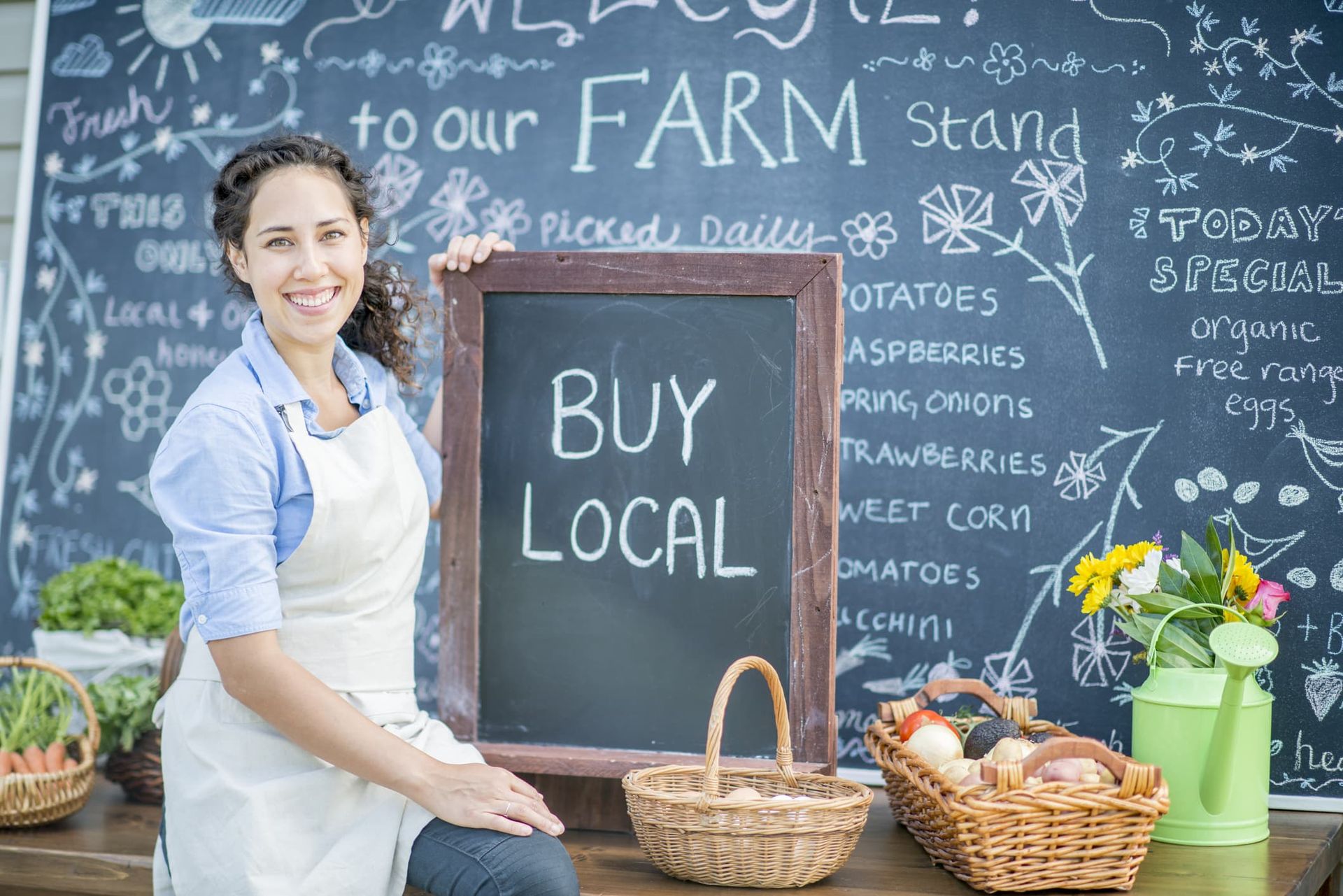 A woman is standing in front of a chalkboard holding a sign that says `` buy local ''.
