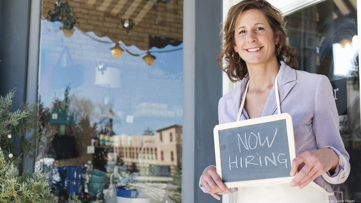 A woman is holding a sign that says `` now hiring ''.