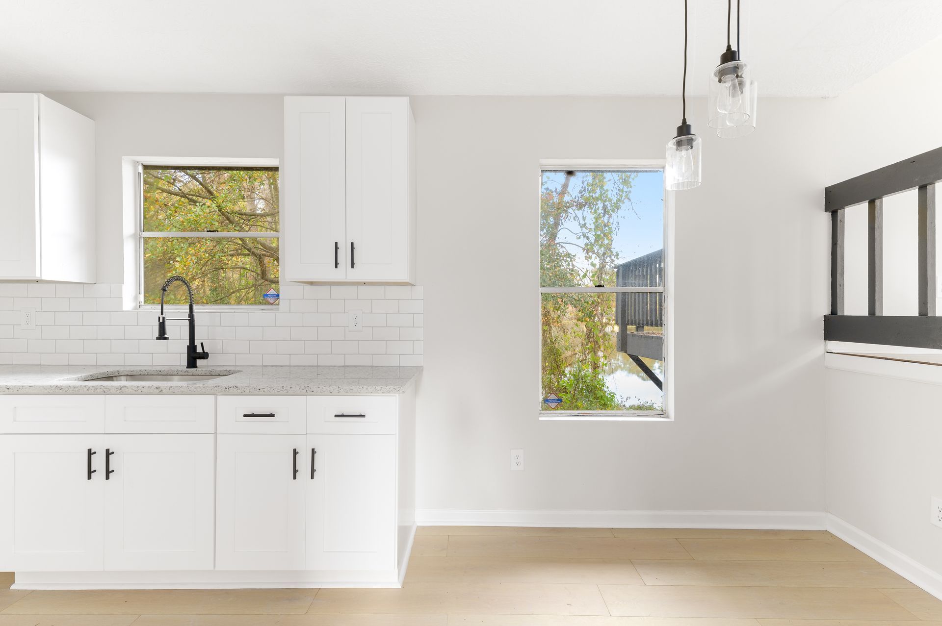 An empty kitchen with white cabinets , a sink , and a window.