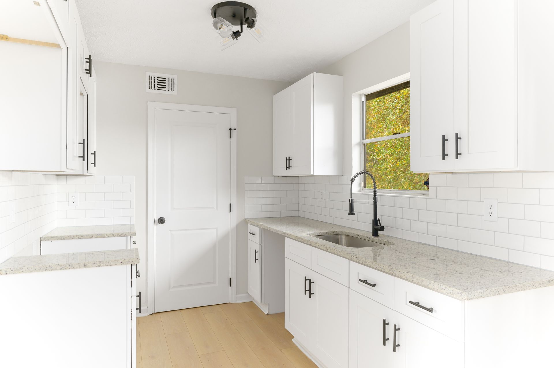 A kitchen with white cabinets , granite counter tops , a sink and a window.