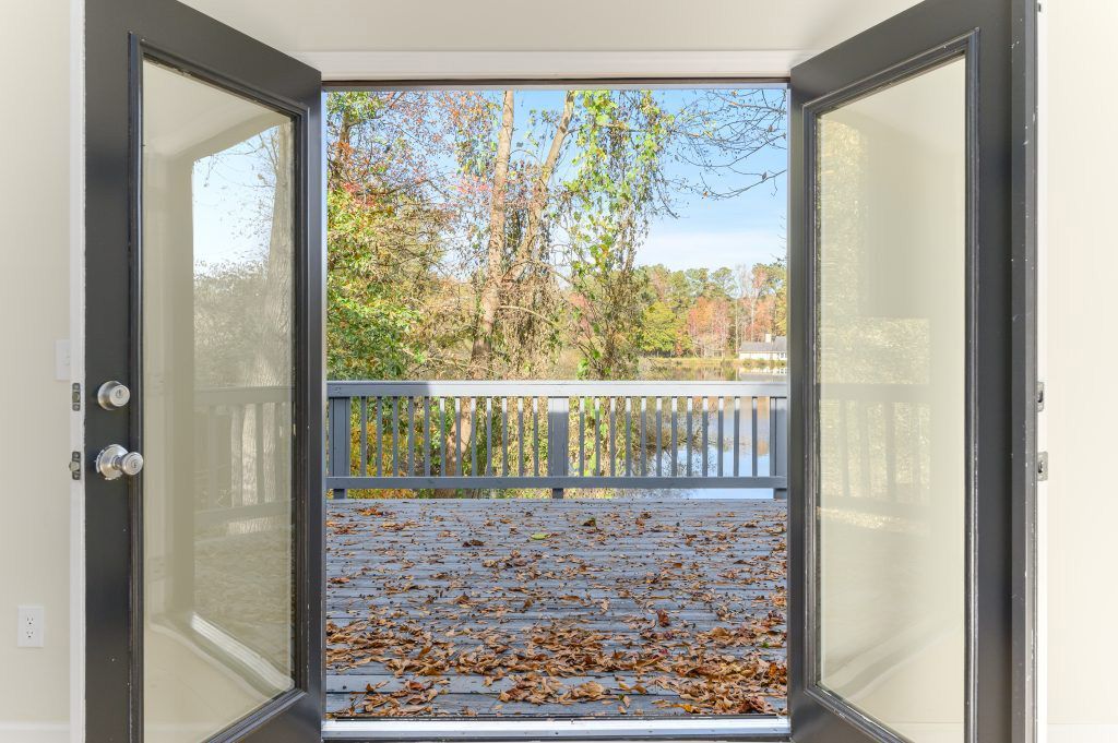 A view of a lake through an open window with leaves on the ground.