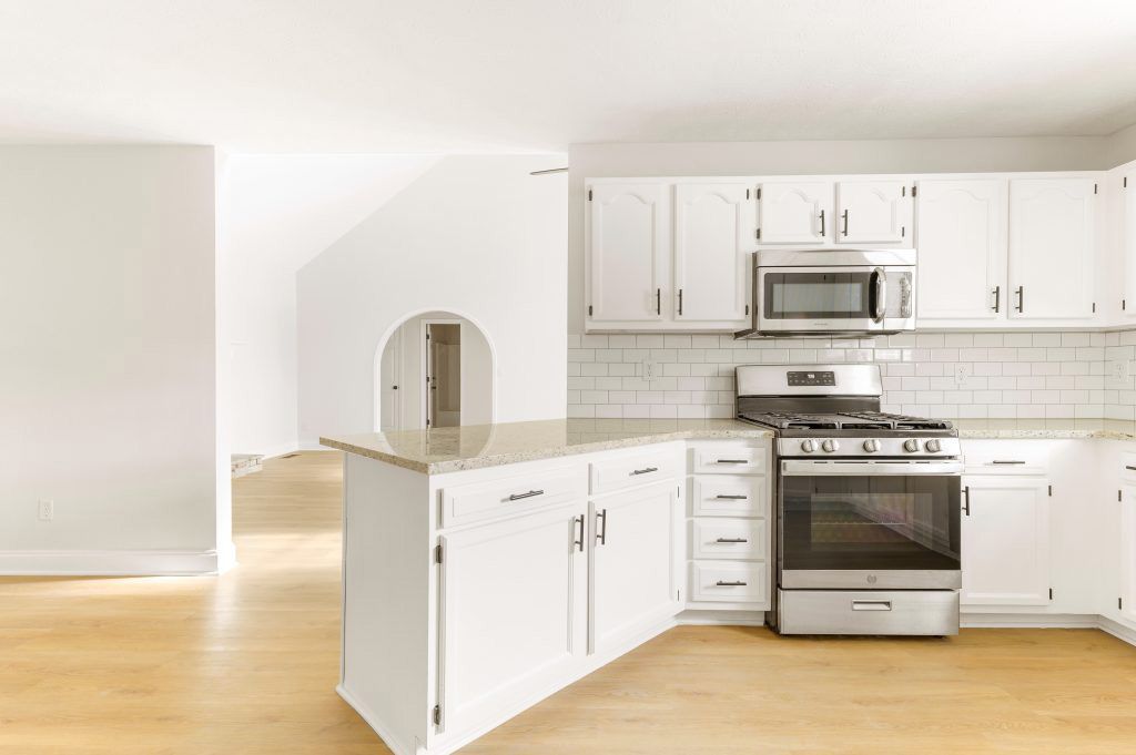 An empty kitchen with white cabinets and stainless steel appliances.