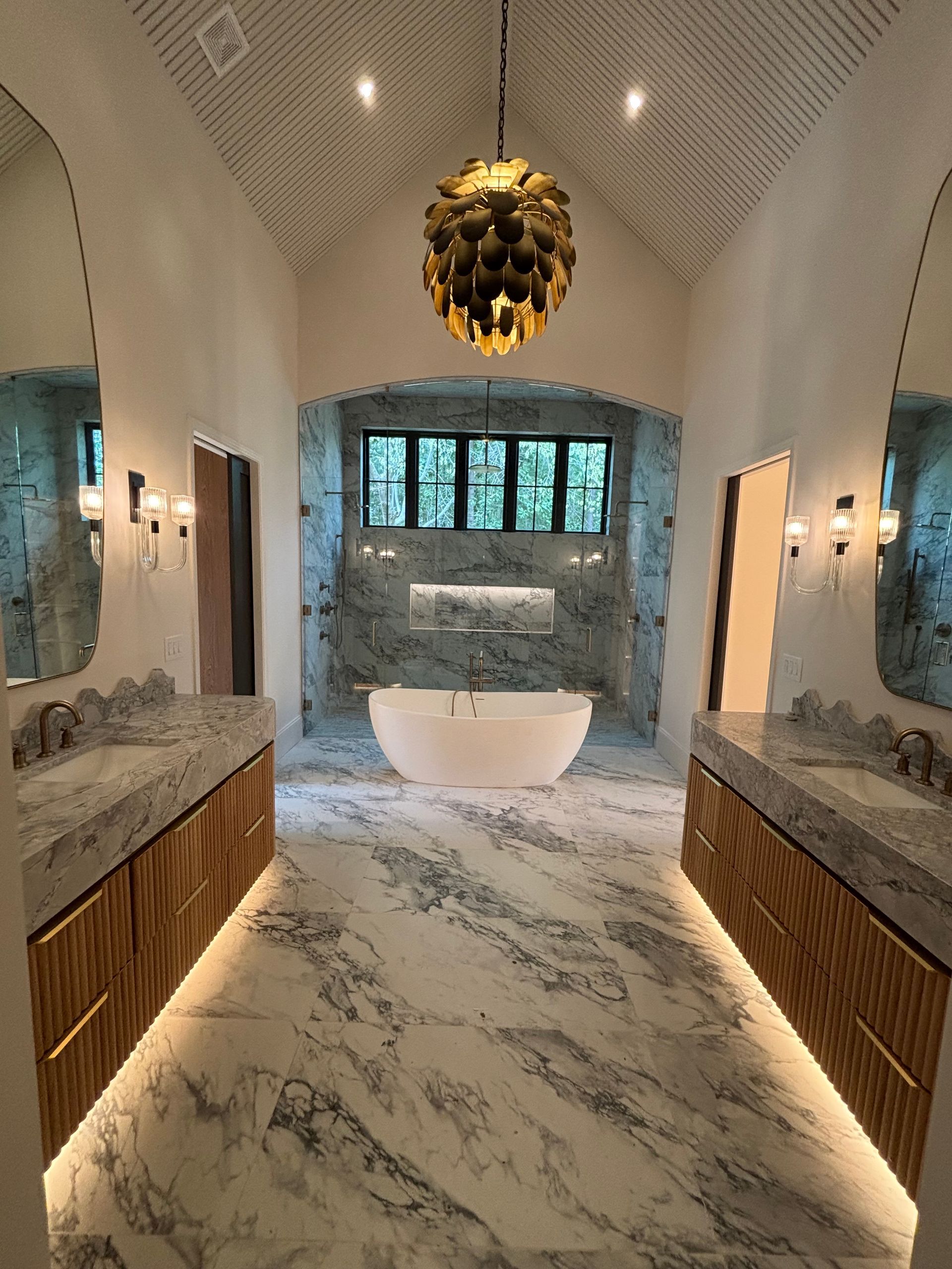 A bathroom with a bathtub , sinks , mirrors and a chandelier hanging from the ceiling.