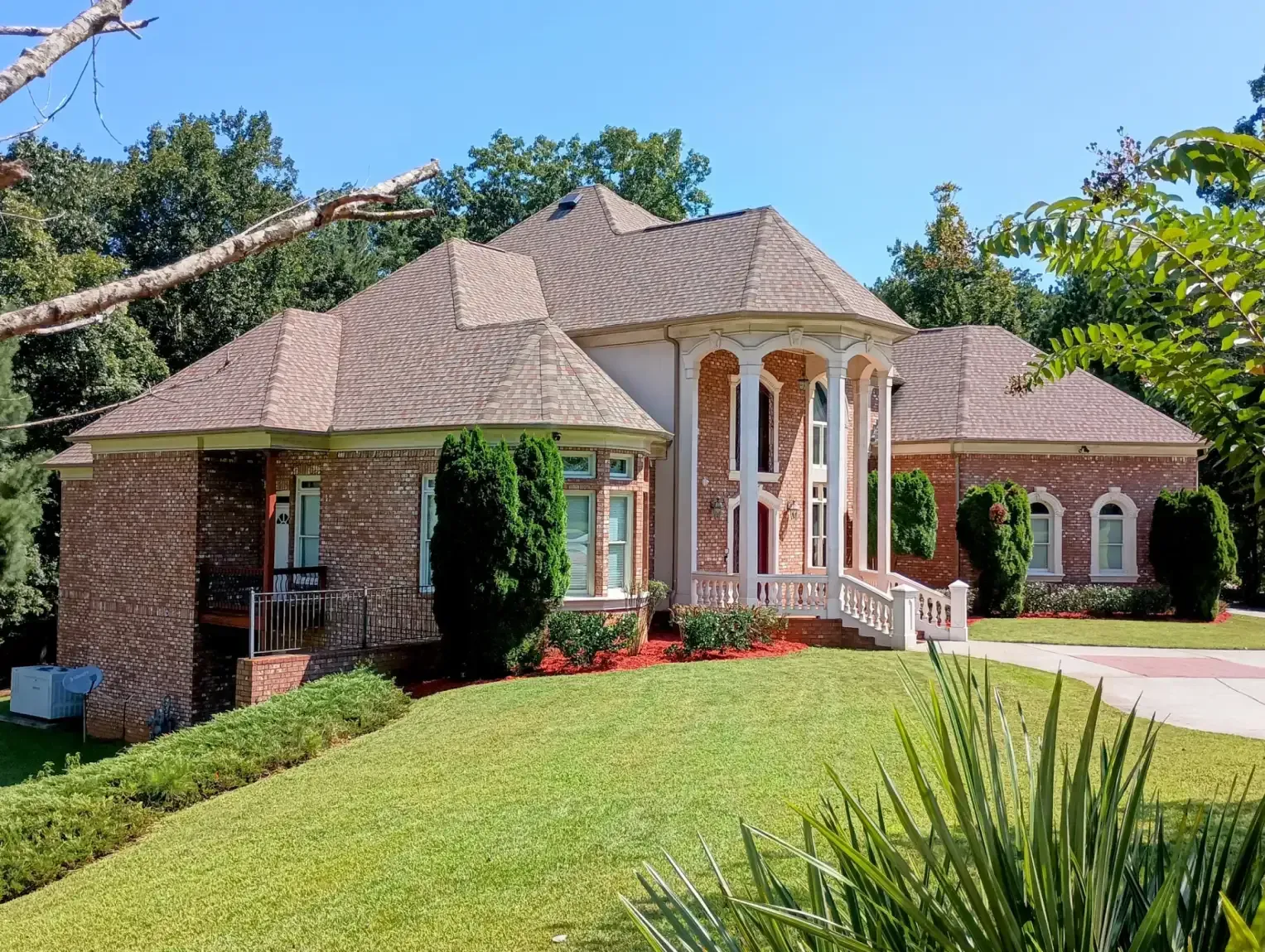 A large, multi-story brick home with a prominent arched white portico, surrounded by green lawns and trees.