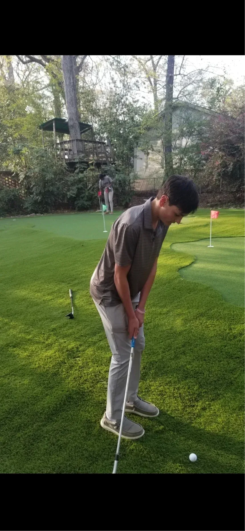 A person stands on a backyard putting green, preparing to putt a golf ball towards a flag.