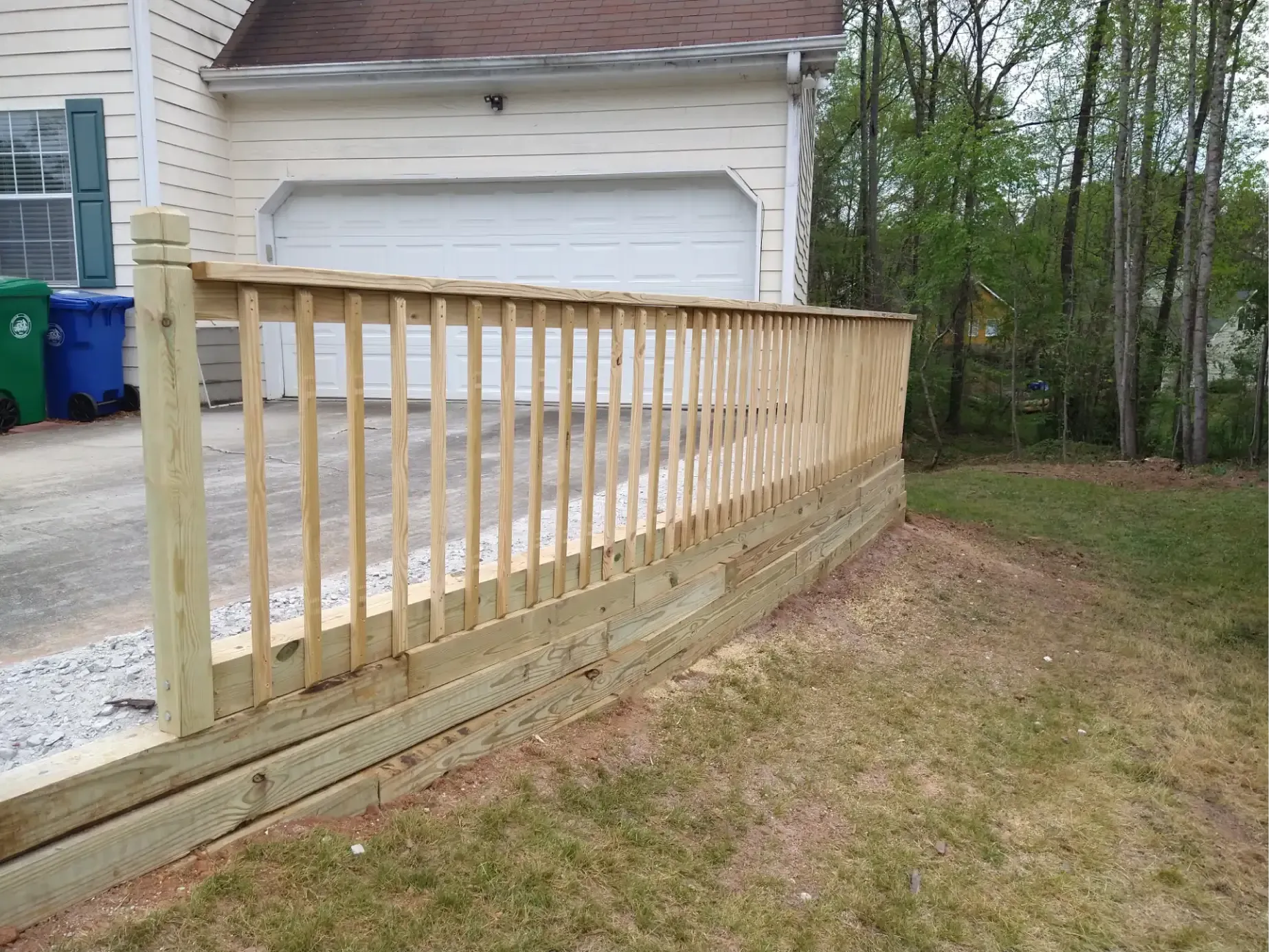 A newly constructed wooden retaining wall and fence bordering a concrete driveway and a grassy yard.